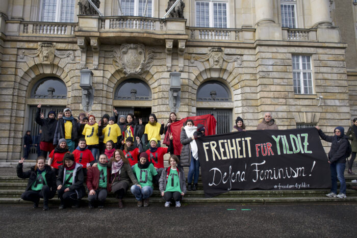 Transparent mit der Aufschrift Freiheit für Yildiz und Aktivist*innen mit Tshirts in den Kurdischen Farben