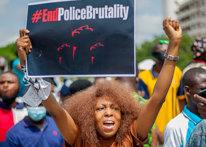 Eine Frau hält bei einer Demonstration ein Schild hoch, auf dem "End Police Brutality" steht und hebt die Faust