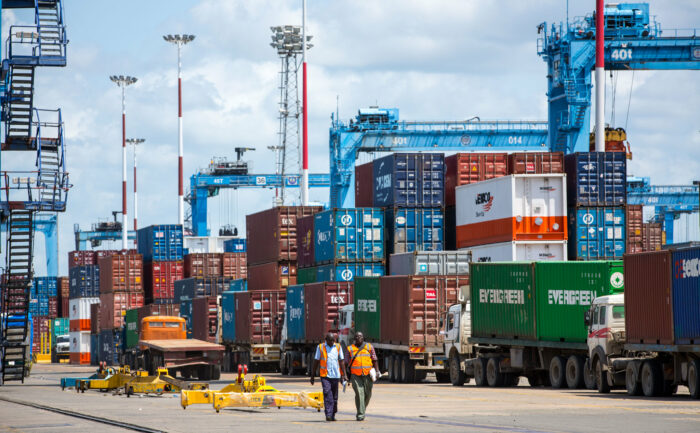 Container und Kräne, zwei Arbeiter laufen im Vordergrund