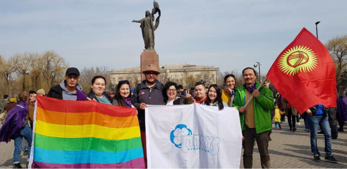 Aktivist:innen posieren mit Krigisischer und LGBT-Flagge vor einer Statue