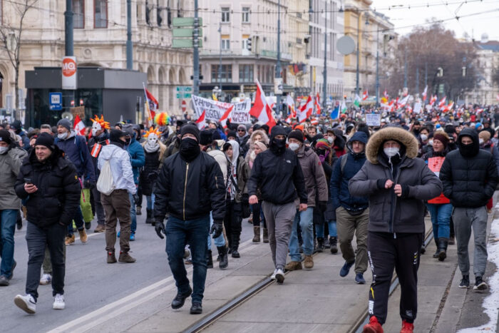 Eine Demonstration mit vielen Österreich-Flaggen. Im Vordergrund bedrohlich aussehende, maskierte Männer
