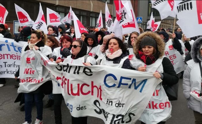 Arbeiterinnen mit ver.di-Westen, Fahnen, Trillerpfeifen und Banner.