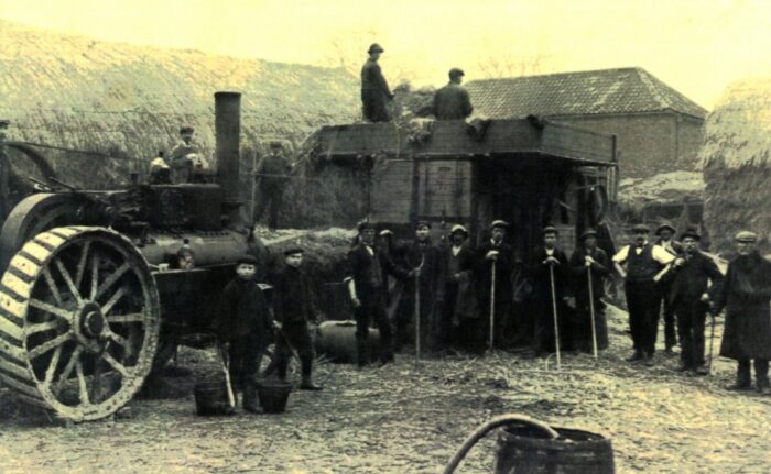 Schwarzweiß Foto von Landarbeitern sowie Kindern, die mit Heugabeln auf einem Hof stehen.