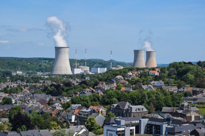 Bild eines Ortes in einer hügeligen Landschaft, im Hintergrund drei Schornsteine eines Atomkraftwerks.