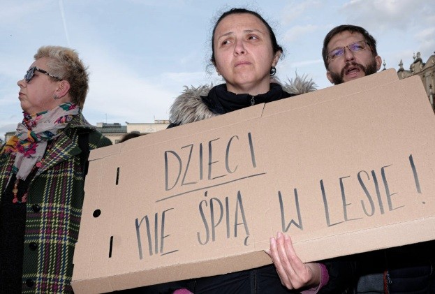 Drei Menschen halten ein Pappschild mit der Aufschrift "dzieci nie śpią w lesie"