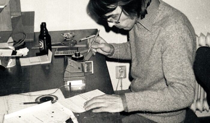 Schwarzweißaufnahme eines Mannes, der am Schreibtisch sitzt, einen Bleistift in der Hand hält und sich über einige Zettel beugt
