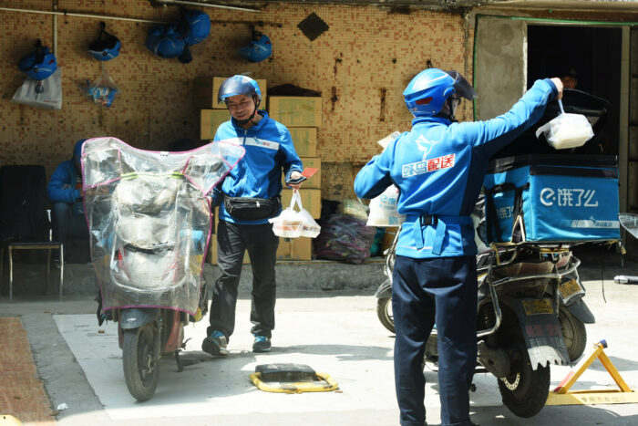 Zwei Essenskuriere laden Tüten mit Lieferungen in die Transportboxen ihrer Motorräder