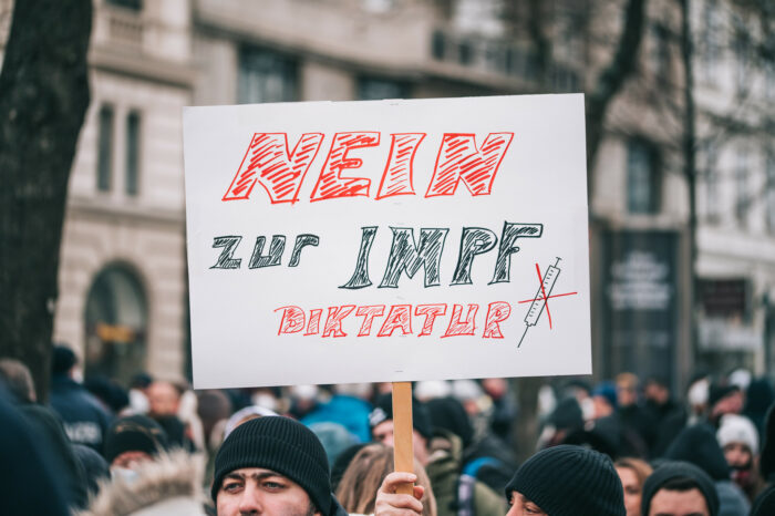 Demoszene, das halbe Gesicht eines Mannes mit Mütze ist zu sehen, daneben ein Schild mit der Aufschrift "Nein zur Impf-Diktatur"