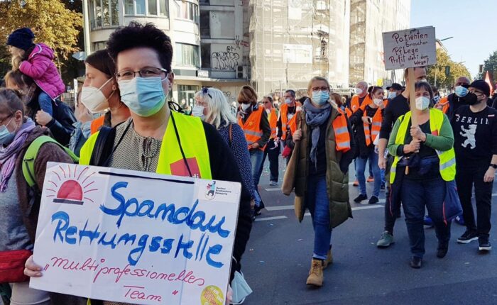 Bei einem Protest der Berliner Krankenhausbewegung trägt eine Person ein Schild um den Hals, auf dem steht "Spandau Rettungsstelle".