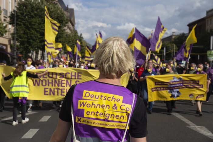 Eine Person in "Deutsche Wohnen & Co enteignen" Weste von hinten, wie sie auf die Spitze einer Demonstration schaut