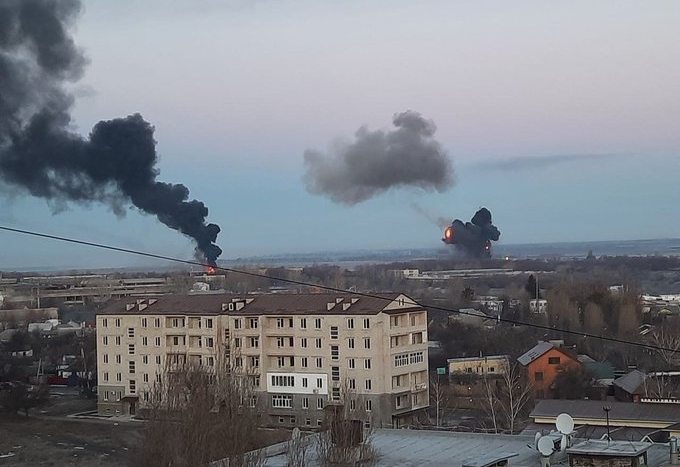 Eine Landschaft mit größeren Wohnhaus und einigen kleineren Häusern im Morgengrauen, an zwei Orten steigen dunkle Rauchsäulen auf