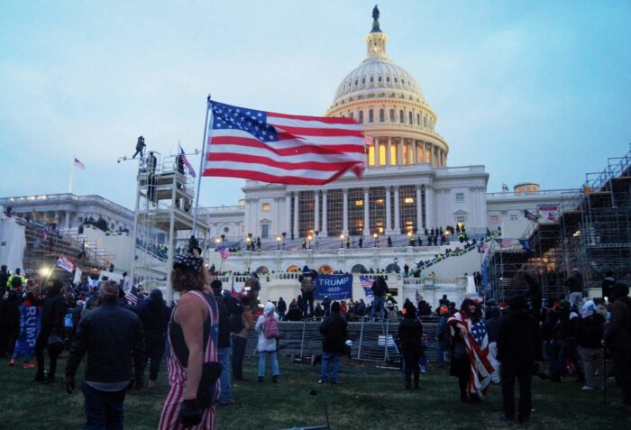 Vor dem Kapital steht in der Dämmerung eine verstreute Menschenmenge, viele schwenken USA-Flaggen oder Trump-Banner