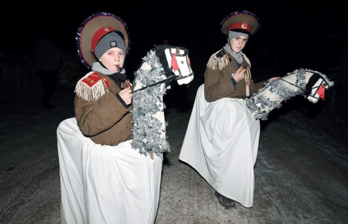 Zwei junge Menschen in Uniformen auf gebastelten Pferden auf einem schneebedeckten Weg in nächtlicher Umgebung