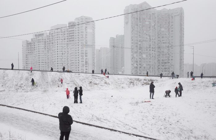 Menschen rodeln auf einem verschneiten Abhang vor Hochäusern