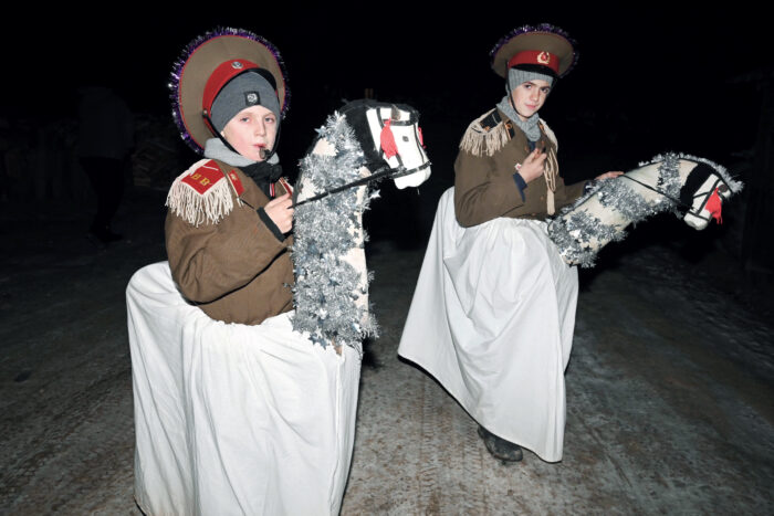Zwei junge Menschen in Uniformen auf gebastelten Pferden auf einem schneebedeckten Weg in nächtlicher Umgebung