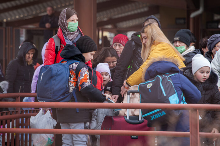 Eine Gruppe Frauen unterschiedlichen Alters und Kinder stehen mit Gepäck an einer Metallabsperrung