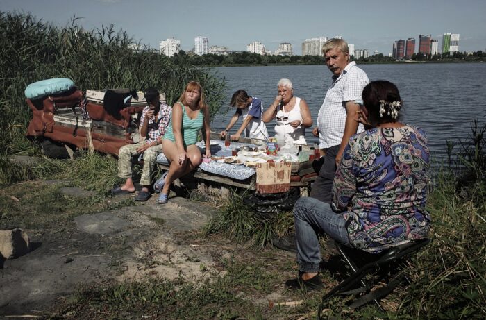 Eine Familie, teils in Badeklamotten, sitzt an einem See und macht Picknick