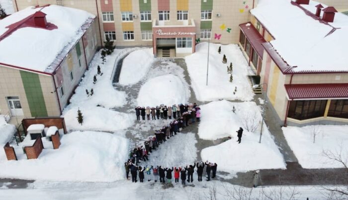 Menschen bilden vor einem Gebäude auf einem schneebedeckten Platz ein Z.