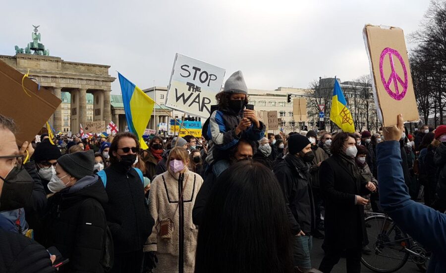 Man sieht Menschen am Brandenburger Tor mit Ukraine-Fahnen und ein Pappschild: Stop the War.