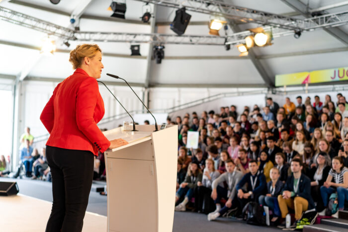 Franiska Giffey spricht lächelnd von einem Podium mit einer Gruppe Zuhörenden.