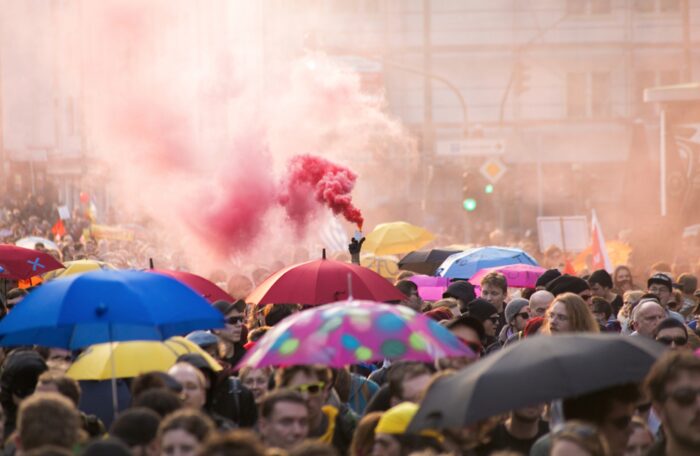 Demonstrant*innen unter Regenschirmen, über dem Demonstrationszug steigt rauch auf, jemand hält einen Bengalo in die Höhe