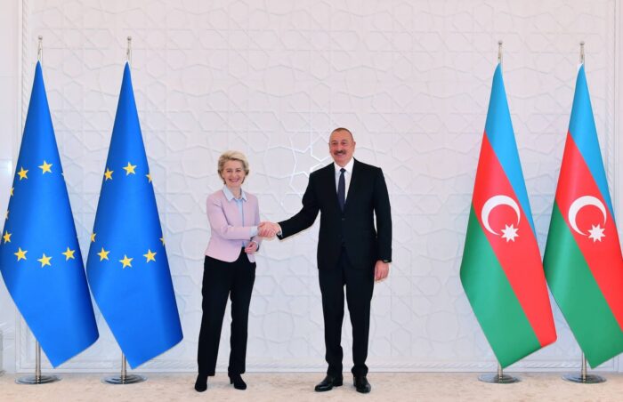 Ursula von der Leyen und Ilham Aliyev schütteln Hände, eingerahmt von Flaggen der EU und Aserbaidschans