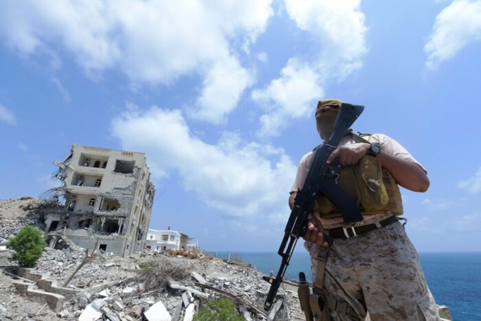 Man sieht ein zerstörtes Gebäude vor blauem Himmel, vor dem ein Soldat steht.