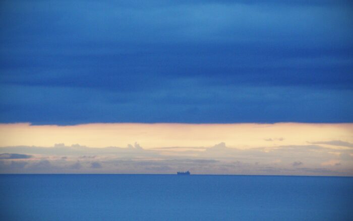 Das Meer mit Blick auf den Horizont; wo sich Himmel und Meer begegnen, ist ein Schiff zu sehen