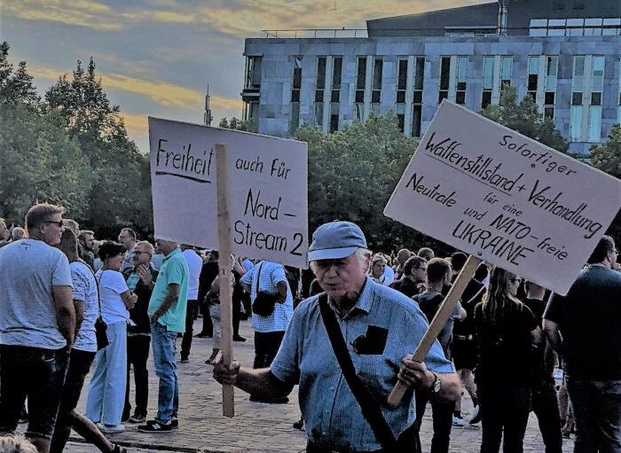 Ein älterer Mann trägt zwei Schilder in seinen Händen. Auf dem einen Schild steht »Freiheit auch für Nord-Stream 2«. Auf dem anderen Schild steht: »Sofortiger Waffenstillstand + Verhandlung für eine Neutrale und NATO-freie UKRAINE«.