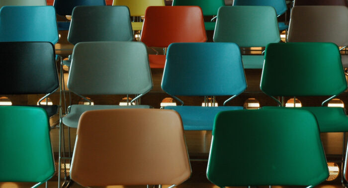 Hintereinander aufsteigend geordnete und bunte Stühle in einer Vorlesungshalle