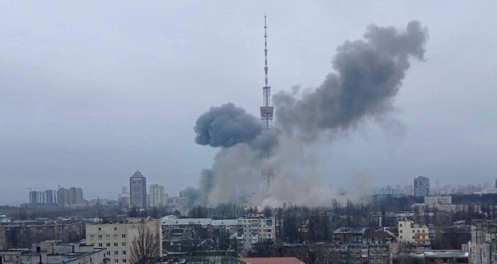 Bild einer Stadt, in der Mitte ein Fernsehturm mitten in einer Rauchsäule infolge eines Raketenagriffs