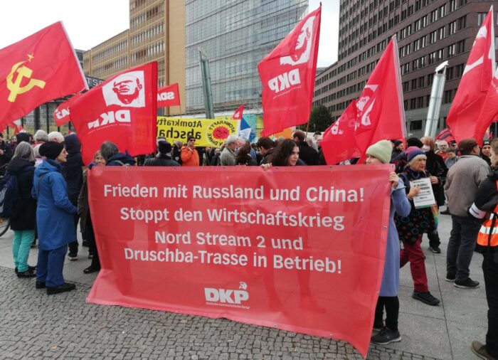 Man sieht mehrere Leute, die Fahnen der DKP halten sowie ein Banner, auf dem steht: Frieden mit Russland und China! Stoppt den Wirtschaftskrieg, Nordstream 2 und Druschba-Trasse in Betrieb! DKP