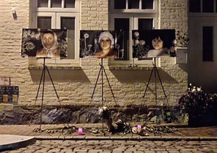 Einer Häuserwand mit drei davor augestellten Bildern, der Opfer, darunter Kränze
