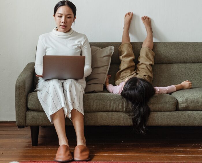 Mutter mit Laptop und Kind auf einem Sofa.