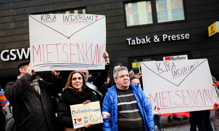 Drei Menschen auf einer Demonstration. Mehrere von ihnen halten Schilder hoch. Aufschrift: "Kira Indirimi! / Mietsenkung". Auf einem Briefumschlag steht: Mietminderungen an die GSW