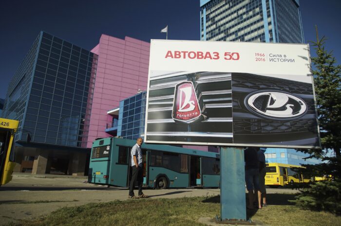 Eine Werbetafel für ein Auto, dahinter ein Mann, mehrere Busse und mehrere Gebäude