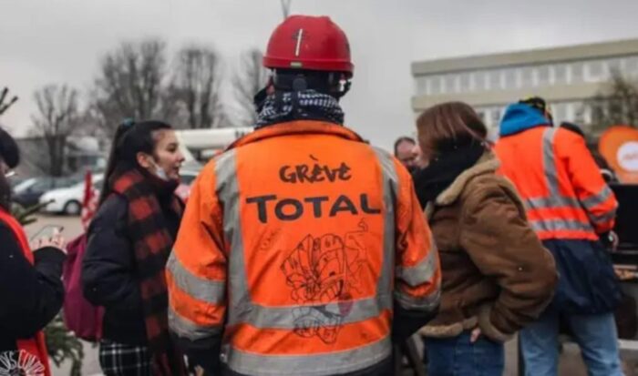 Man sieht einen Arbeiter mit rotem Helm und Oranger Jacke auf der steht Greve Total - totaler Streik.