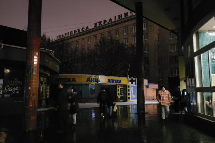 Straßenszene, ein dunkler Platz, dahinter ein dunkles Haus, von der rechten Seite fällt Licht auf einen Fußgänger