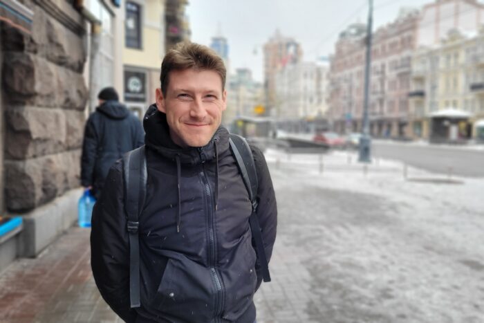 Ein junger Mann steht auf einer verschneiten Straße und lächelt in die Kamera