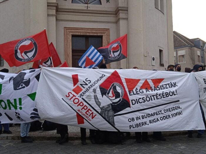 Ausschnitt eines Demo-Blocks hinter mehreren Bannern, wo unter annderem steht "NS-Verherrlichung stoppen" und Antifa-Flaggen.