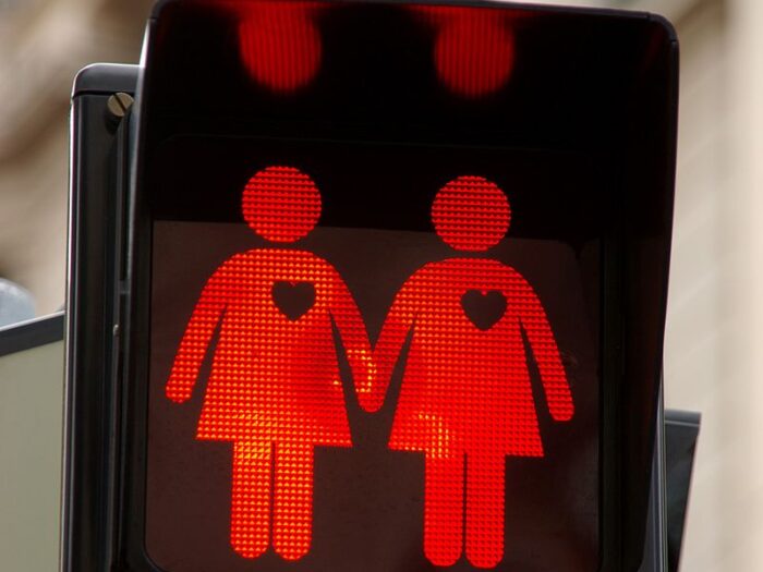 Pictogramm einer Ampel, auf der zwei Menschen in Kleidern sich die Hände halten und mit Herzchen