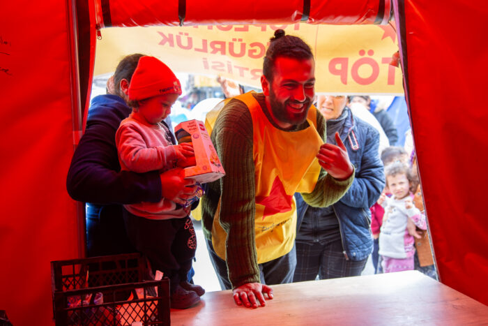 Man sieht eine Person mit gelber Weste an einem Stand und ein Kind.