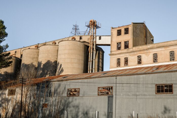 Bild eines alten, verlassenen Silos mit den Silo tanks links, verbunden zu einem Verarbeitungsgebäude rechts.