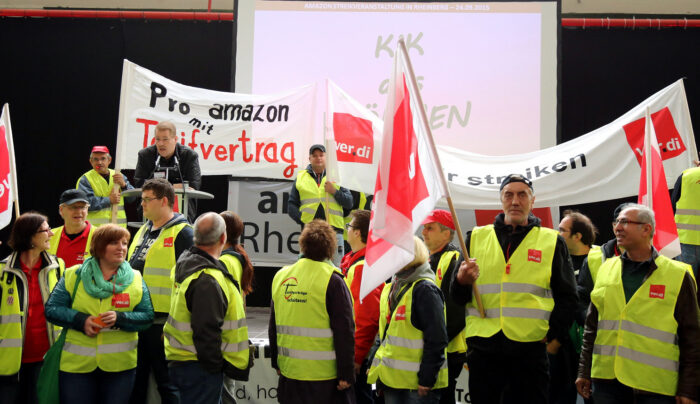 Eine Gruppe Menschen in Warnwesten und mit verdi-Fahnen, zwei Transparente sind zu sehen, auf einem steht "pro amazon mit Tarifvertrag" und auf dem anderen "Wir streiken"