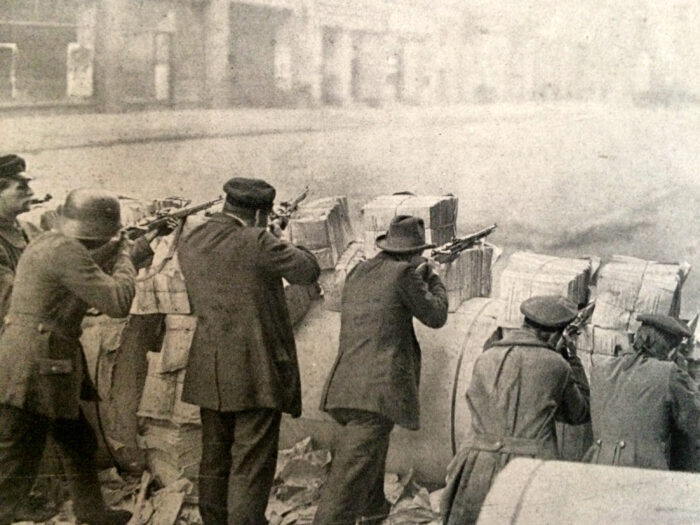 Von hinten fotografierte Person, an einer Barrikade, die dort ihre Gewehre aufgelegt haben und zielen