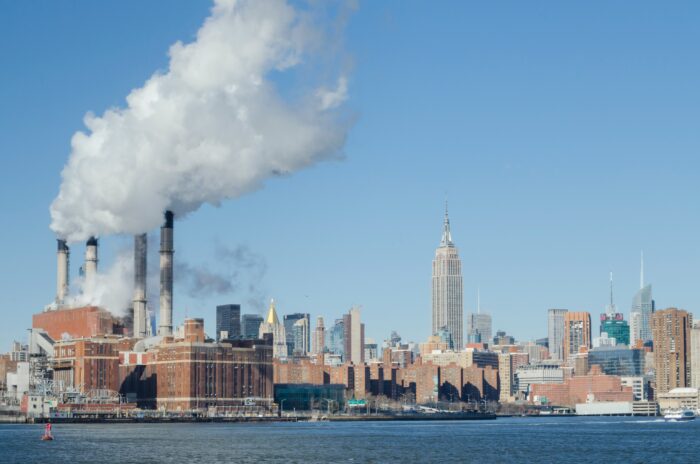 Rauchende Schornsteine in New York, im Vordergrund das Meer.