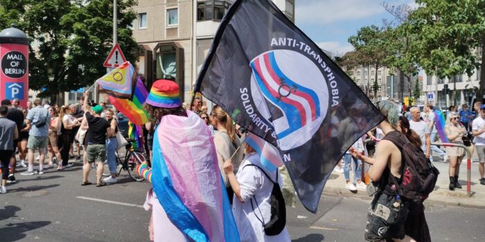 Menschen auf einer Demo mit einer Fahne, auf der steht "Anti-Transphobia - Solidarität"