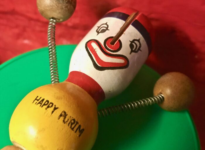 Eine bunte Holzpuppe mit Clownsgesicht, darauf steht "Happy Purim".