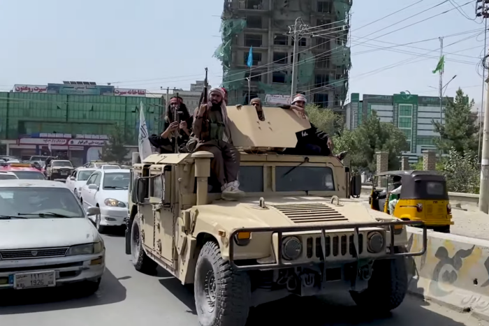 Taliban-Kämpfer sitzen auf einem in einem von ihnen übernommenen US-Militärfahrzeug. Um sie herum normaler Verkehr.