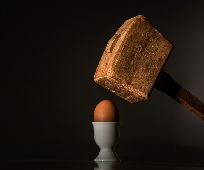 Ein großer Holzhammer fällt auf ein ein in einem Eierbecher